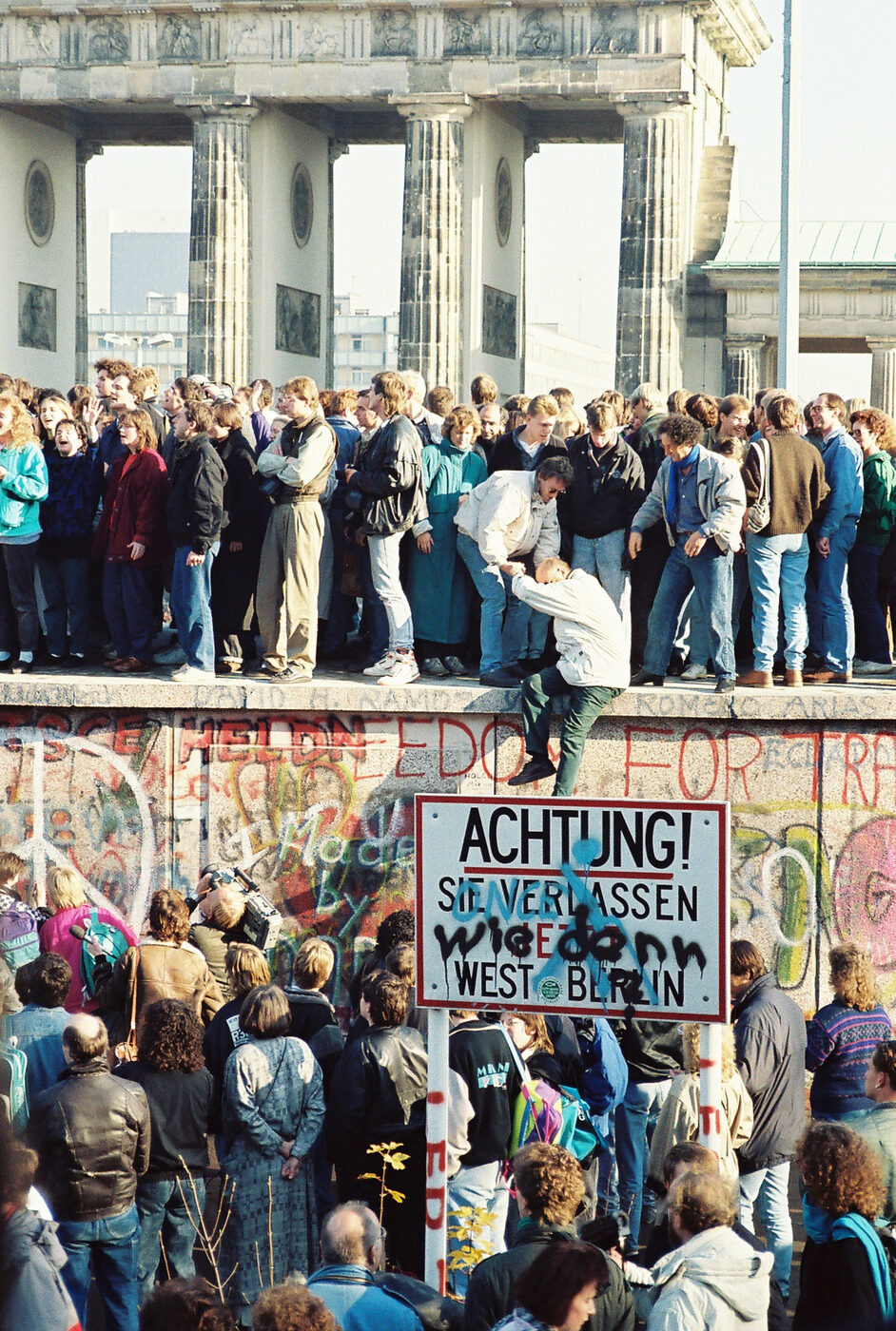 Crowds standing on top of the Berlin Wall in front of the Brandenburg Gate as the border opens in November 1989