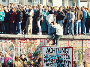 Folle in piedi sulla sommità del Muro di Berlino davanti alla Porta di Brandeburgo mentre il confine si apre nel novembre 1989