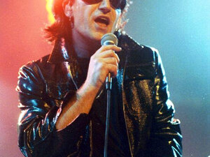 Bono degli U2 nei panni del suo personaggio The Fly durante lo Zoo TV Tour del 1992, in occhiali da sole e pelle, mentre canta al microfono